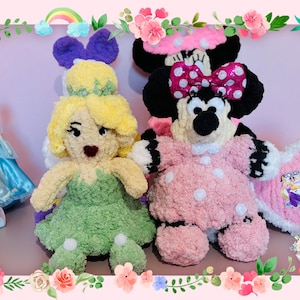 May include: Handmade crochet dolls of Tinkerbell and Minnie Mouse, with a Cinderella doll in the background. The Tinkerbell doll wears a green dress and yellow hair. Minnie Mouse is in a pink polka-dot dress and bow.