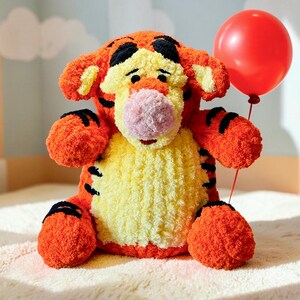 Puede incluir: Un peluche de tigre con pelaje naranja y amarillo, rayas negras y una nariz rosa. El personaje tiene una cabeza redonda, orejas grandes y una textura suave. Sostiene un globo rojo brillante sujeto por un hilo fino en su mano derecha.