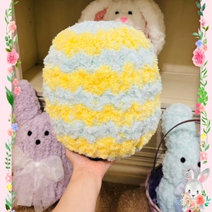 May include: A yellow and blue striped plush Easter egg with a fuzzy texture. The egg is being held by a hand in front of a shelf with plush bunnies.