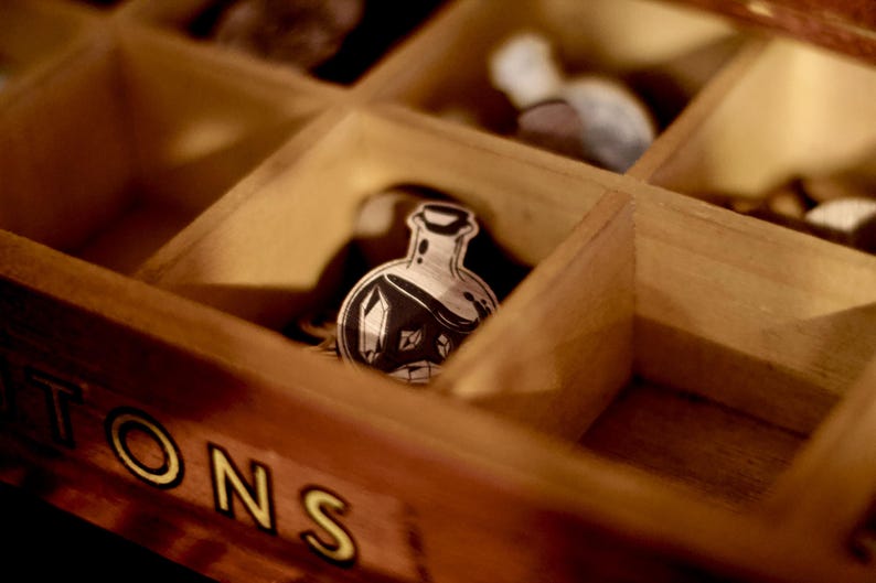 May include: A wooden box with compartments, each containing a small, black and white illustration of a potion bottle. The box is labeled "TONS" in yellow letters.