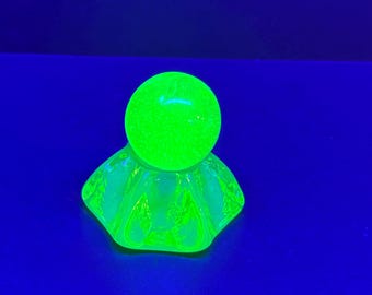 May include: A glowing green glass object with a round top and a hexagonal base. The glass has a textured appearance and is illuminated against a dark blue background. The object appears to be a decorative item.