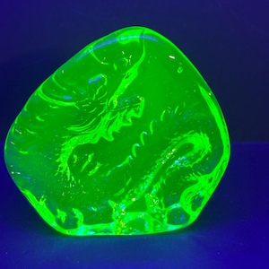 May include: A bright green glass paperweight with a swirling, abstract design. The glass is translucent and has a slightly cloudy appearance.