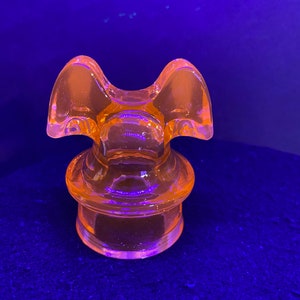 May include: A bright orange glass bottle stopper with a unique, whimsical design. The stopper has two rounded wings and a round base.