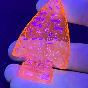 May include: A light orange arrowhead with a textured surface, glowing under a black light.