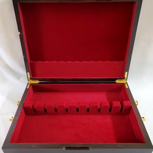 May include: A rectangular dark wood storage box with a hinged lid, featuring a vibrant red velvet interior lining. The box includes a built-in red velvet rack with ten slots for organizing items, complemented by polished gold-tone metal hinges.