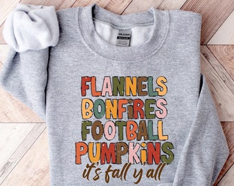 Könnte beinhalten: Grauer Pullover mit einem bunten Grafikdruck, auf dem "Flannels, Bonfires, Football, Pumpkins, it's fall y'all" steht.