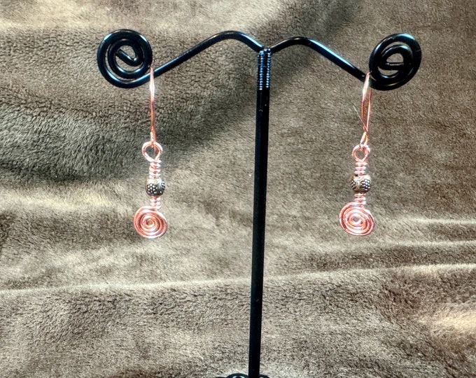 Handmade +  1 1/4” copper wire earrings tightly woven into a small spiral with a small copper bead hanging on handmade French ear wires. Gif