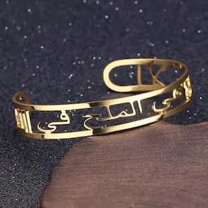 Peut inclure: Bracelet jonc doré avec une inscription en arabe. L'inscription est découpée dans le métal, créant un design délicat et complexe.