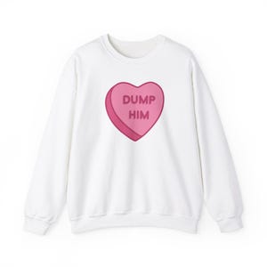Puede incluir: Sudadera blanca con un gráfico de caramelo en forma de corazón rosa que dice "DUMP HIM" en letras rosas.