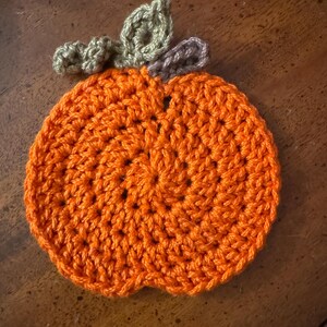 May include: A crocheted pumpkin coaster in orange with green and brown leaves.