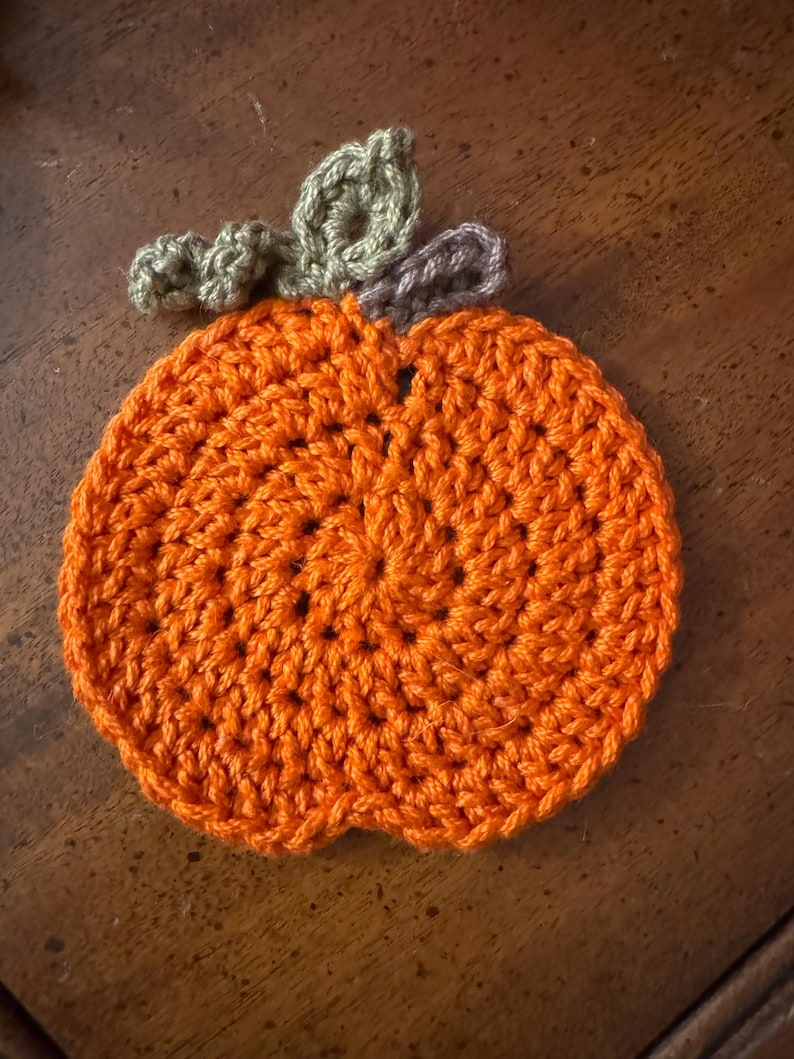 May include: A crocheted pumpkin coaster in orange with green and brown leaves.