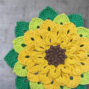 May include: A handmade crochet sunflower with a brown center, surrounded by yellow petals. The petals are framed by green and light green leaves, creating a vibrant, textured floral design. This item is perfect for home decor.