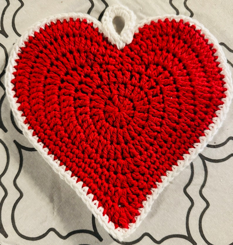 May include: A red crocheted heart-shaped pot holder with a white crocheted border and a loop at the top.