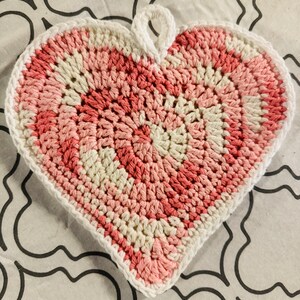 May include: A crocheted heart-shaped pot holder in pink and white.