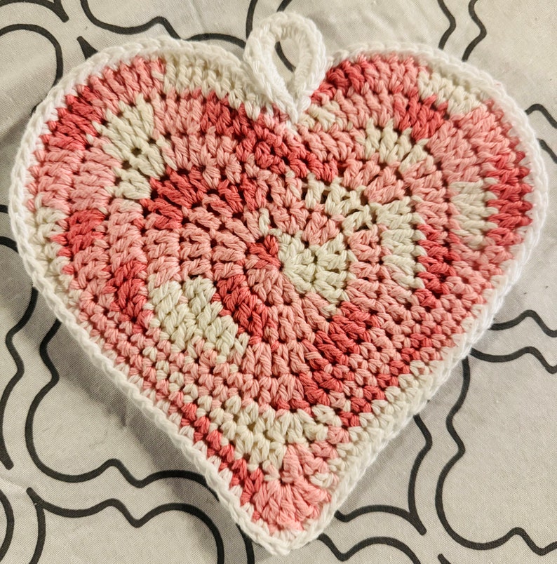 May include: A crocheted heart-shaped pot holder in pink and white.
