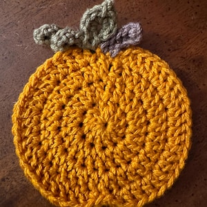 May include: A crocheted pumpkin coaster in orange with green and purple leaves.
