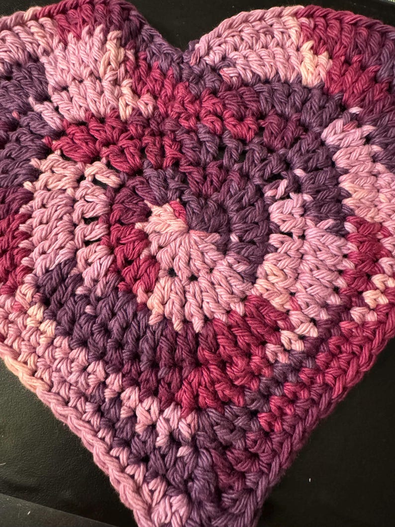May include: A heart-shaped crocheted dishcloth in shades of pink, purple, and burgundy.