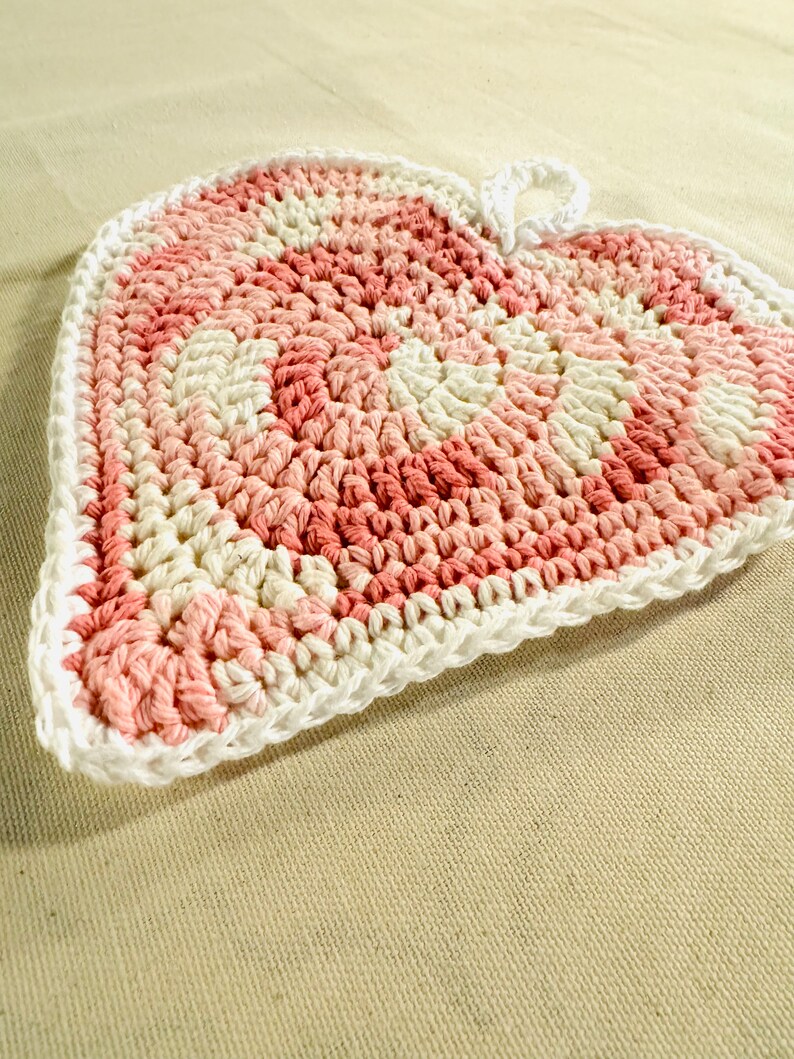 May include: A pink and white crocheted heart-shaped pot holder with a loop for hanging.