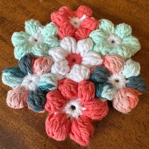May include: A crocheted flower coaster with a variety of colors, including pink, white, green, and teal.