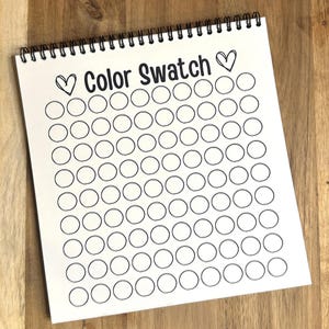 May include: A white spiral bound book with the title "Color Swatch" and a heart on either side of the title. The book has 10 rows of 10 blank circles, each with a black outline.