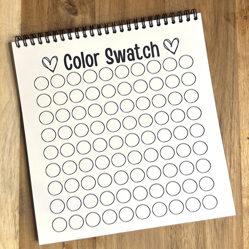 May include: A white spiral bound book with the title "Color Swatch" and a heart on either side of the title. The book has 10 rows of 10 blank circles, each with a black outline.
