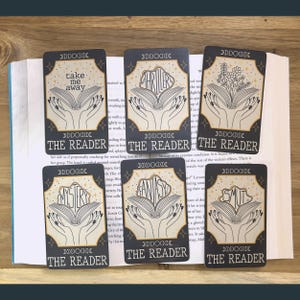 May include: Set of ten black and gold tarot cards with illustrations of open books and the words "The Reader" and different genres of literature, such as "Mystery", "Fantasy", "Thriller", "Smut", and "Take Me Away".