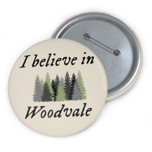 May include: A cream-colored button with a black and white graphic that says "I believe in Woodvale" with a row of green and gray trees below the text.