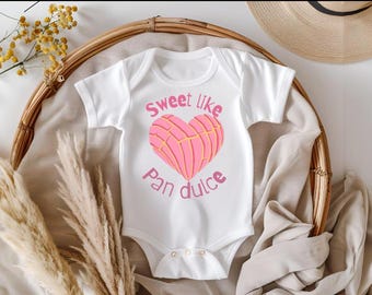 May include: White baby onesie with a pink heart-shaped pan dulce illustration and the text "Sweet like Pan Dulce".