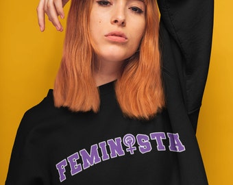 May include: Black sweatshirt with a purple feminist symbol and the word "FEMINISTA" printed on the front.