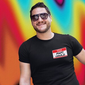 May include: A black t-shirt with a red name tag that says "Hola, me llamo Papi Chulo".