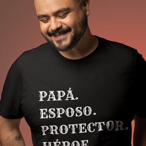 May include: A man wearing a black t-shirt with the words "PAPÁ. ESPOSO. PROTECTOR. HÉROE." printed in white.