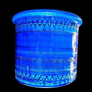 May include: A cylindrical ceramic vessel in a vibrant cobalt blue glaze. The exterior surface features horizontal bands of embossed geometric patterns, including rows of diamonds, vertical lines, and small circles, creating a textured relief.