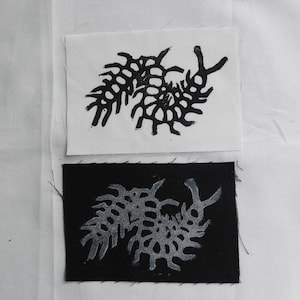 May include: Two fabric squares, one white and one black, each with a black and white print of a stylized centipede design.