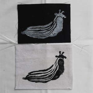 May include: Two fabric swatches with a black and white print of a stylized sea slug. The top swatch is black fabric with a white print. The bottom swatch is white fabric with a black print.