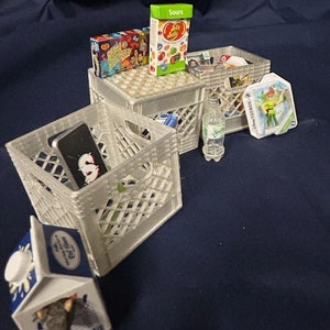 Puede incluir: Tres cajas de plástico blanco llenas de varios artículos, incluyendo dulces, una botella de agua y un pequeño recipiente de plástico con un personaje de dibujos animados. Los artículos están dispuestos sobre una superficie azul.