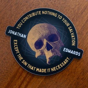 May include: A round sticker with a skull graphic. The skull is tan and purple, with a dark blue background. Text around the edge reads "YOU CONTRIBUTE NOTHING TO YOUR SALVATION" and "EXCEPT THE SIN THAT MADE IT NECESSARY." The name "JONATHAN EDWARDS" is also included.