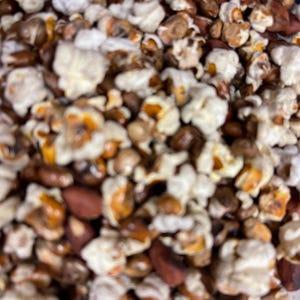May include: A mixture of white, fluffy popped corn kernels and brown, oval-shaped roasted peanuts. The snack mix features a variety of textures, with the light, airy popcorn contrasting against the dense, smooth surfaces of the whole peanuts.
