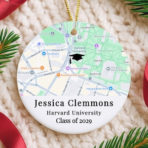 May include: A white ceramic ornament with a map of Harvard University, a black graduation cap icon, and the text "Jessica Clemmons, Harvard University, Class of 2029." The ornament hangs from a gold string.