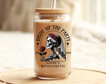 May include: A clear glass jar with a wooden lid and a straw. The jar has a black and white graphic of a skeleton bride with a red rose and the text "Bride of the Party Est 2024 Sarah's Bachelorette".