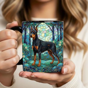 May include: Black coffee mug featuring a Doberman Pinscher illustration in a stained-glass style. The dog is black and tan, set against a backdrop of trees and foliage in shades of blue and green. The mug has a black handle.