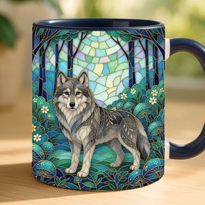May include: A ceramic mug with a dark blue handle and rim, featuring a colorful stained glass style illustration of a grey wolf standing in a forest of blue and green mushrooms and trees with a bright circular light in the background.