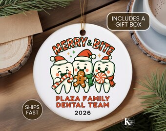 May include: A round white ceramic ornament featuring a graphic of three cartoon teeth wearing Santa hats. The teeth hold a candy cane, a gingerbread man, and a peppermint candy. Text reads MERRY & BITE, PLAZA FAMILY DENTAL TEAM, and 2026.