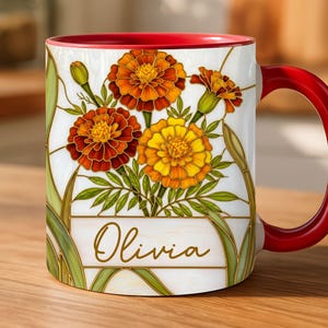 May include: White ceramic mug with a red interior and handle, featuring a floral design of orange and yellow marigold flowers with green leaves. The name "Olivia" is written in gold script on the front.