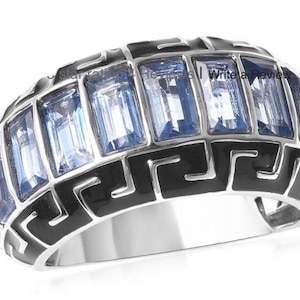 May include: A silver band ring with a black enamel design and blue gemstones. The design features a repeating Greek key pattern.
