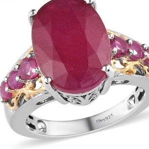 May include: A silver ring with a large oval ruby gemstone surrounded by smaller ruby gemstones. The ring has a gold filigree design and is stamped "D'loy 925".