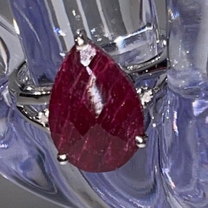 May include: A pear-shaped ruby ring set in silver with small diamonds on the band.