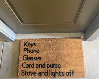 May include: A brown coir doormat with the text "Keys Phone Glasses Card and purse Stove and lights off" printed in black.