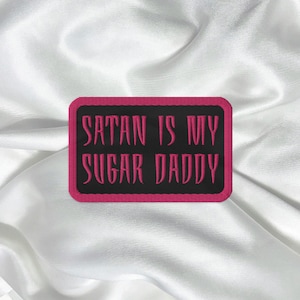May include: A black and pink embroidered patch with the text "Satan is my Sugar Daddy".