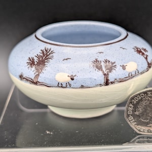 Könnte beinhalten: Eine kleine, runde Keramikschale mit hellblauem Innenraum und cremefarbenem Äußeren. Die Schale ist mit braunen Bäumen und weißen Schafen verziert. Die Schale hat einen Durchmesser von etwa 7,6 cm.