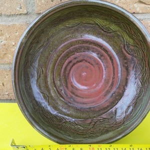 May include: A large, round ceramic bowl with a red and green glaze. The bowl has a swirling pattern in the centre and a wavy design around the rim.
